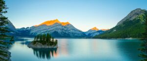Alberta and Rocky Mountains | A golden sunrise illuminating the Kananaskis mountains and lake under a brightening blue sky | Ultimate Travel Company