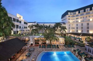Sofitel Legend Metropole | Hanoi | Twilight view of a colonial-style hotel facade with an outdoor pool and patio area | The Ultimate Travel Company
