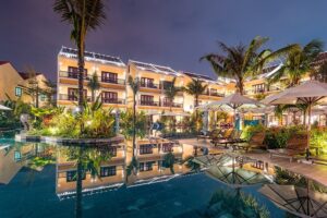 La Siesta Hoi An Resort & Spa | Hoi An | Evening reflection of a tropical hotel and pool with lights and umbrellasl | The Ultimate Travel Company