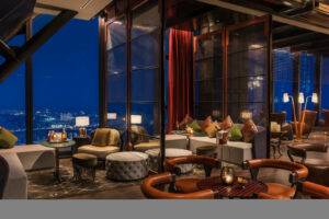 Lounge with City View Through Floor-to-Ceiling Windows at Night in Rosewood Phnom Penh | Luxury Cambodia Holidays | The Ultimate Travel Company