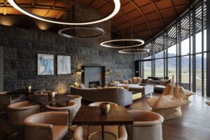 The Lindis, Ahuriri Valley | A modern lounge with circular light fixtures, stone walls, and mountain views | New Zealand | The Ultimate Travel Company