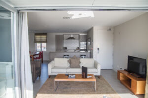 The Waterfront Suites, Bay Of Island | Modern living room with a sofa, TV, and sliding door leading to a balcony | New Zealand | The Ultimate Travel Company