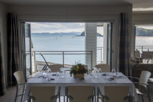 The Waterfront Suites, Bay Of Island | Dining room with a table set for a meal and a view of the sea through large windows | New Zealand | The Ultimate Travel Company