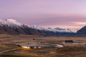 The Lindis, Ahuriri Valley | Twilight over a valley with a lit-up lodge and winding river | The Ultimate Travel Company