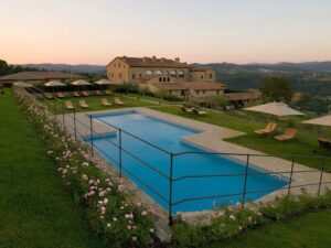 Hotel Le Fontanelle | Tuscany | An outdoor pool with umbrellas and lounge chairs at a Tuscan villa during dusk | The Ultimate Travel Company