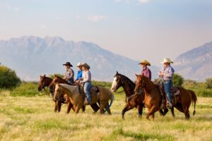 Five People Horseback Riding Across the Grassy Fields with the Mountains of Utah in the Background | Ranch Holidays in the USA | The Ultimate Travel Company